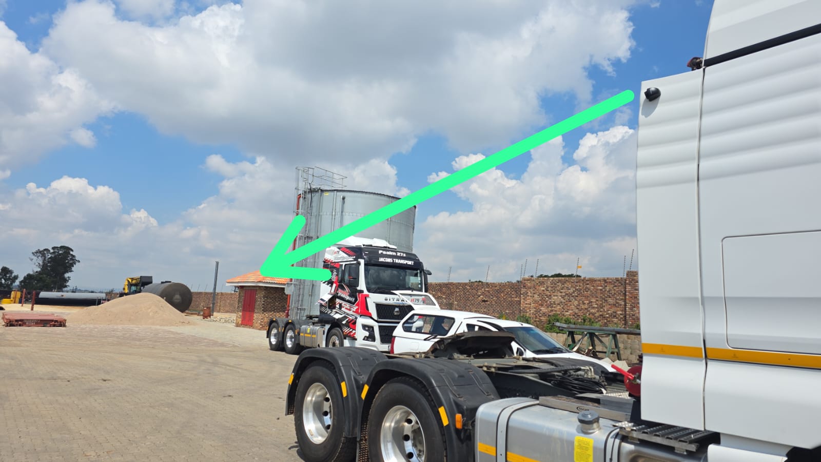 Side view of a Jacobs Transport tractor in a yard with a green arrow indicating the camera mounted on the top-back corner of the cab pointing back along the trailer length